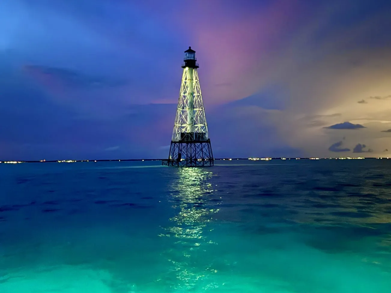Alligator Reef Lighthouse lit up at blue hour, with turquoise water glowing in front of the boat