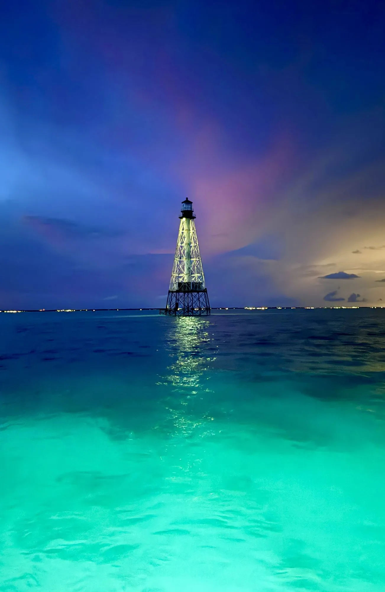 Alligator Reef Lighthouse lit up at blue hour, with turquoise water glowing in front of the boat