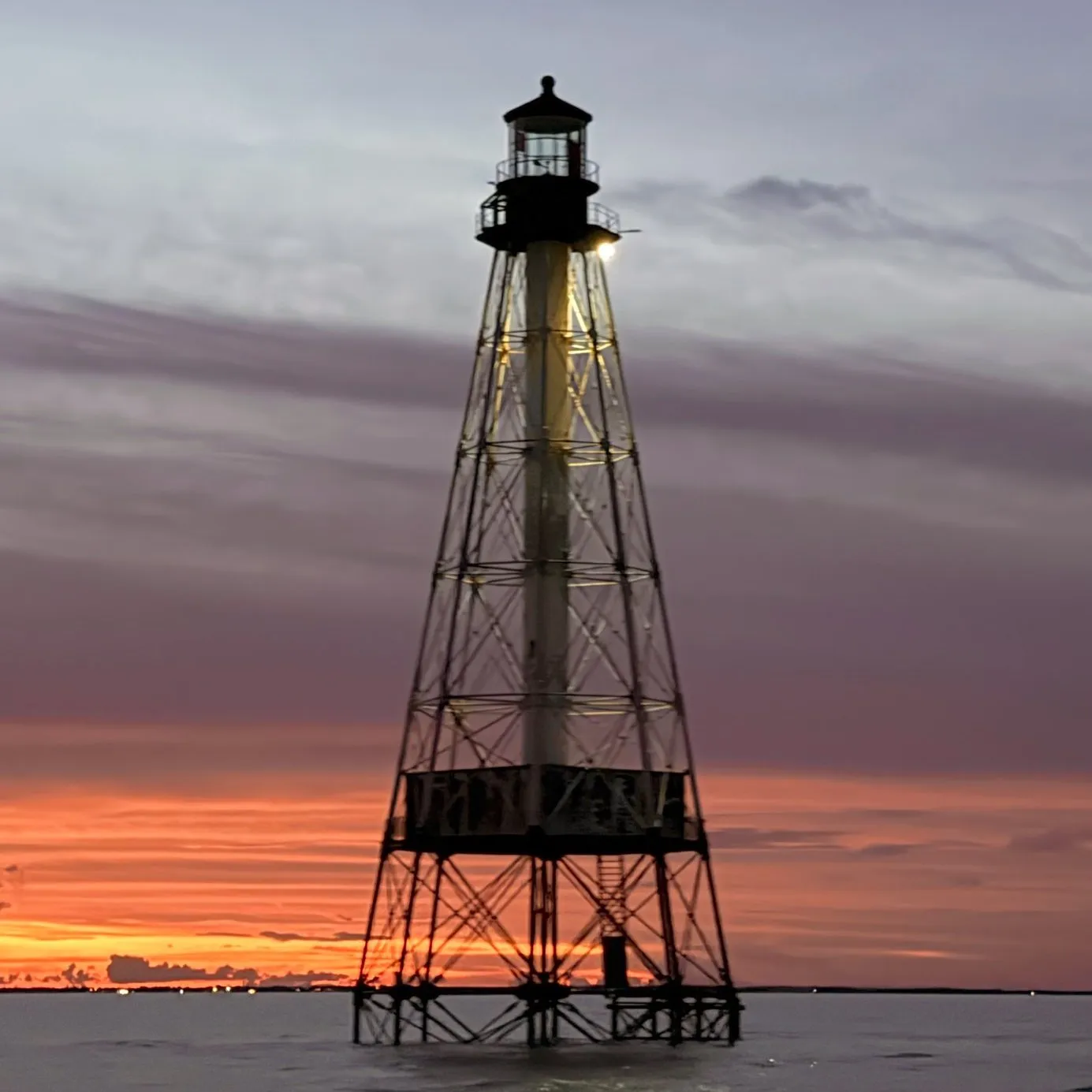 Alligator Reef Lighthouse silhouetted against an orange sunset sky over calm water