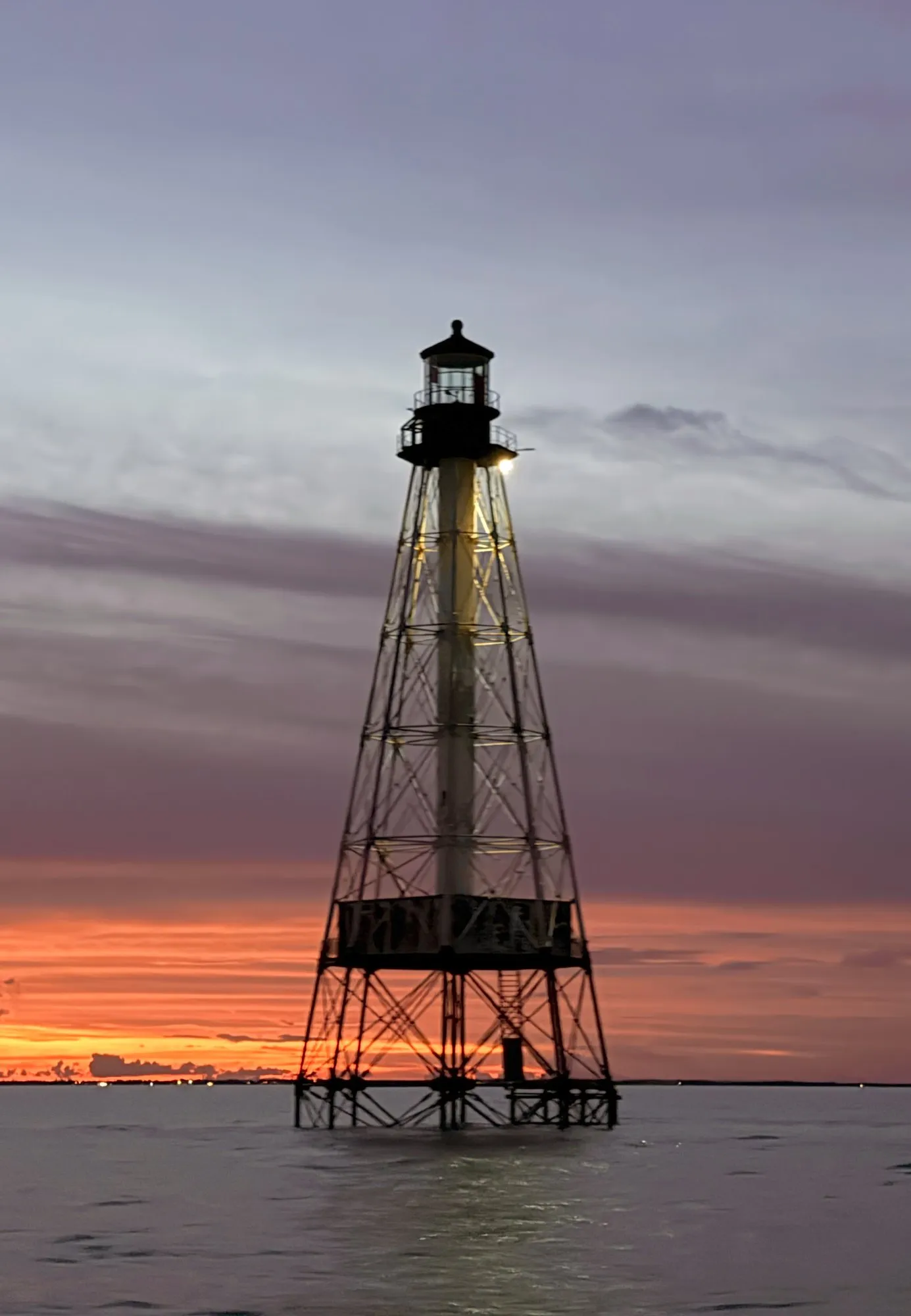 Alligator Reef Lighthouse silhouetted against an orange sunset sky over calm water