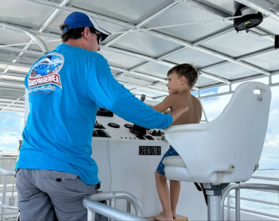 Captain in a Transparensea shirt letting a young guest sit at the helm