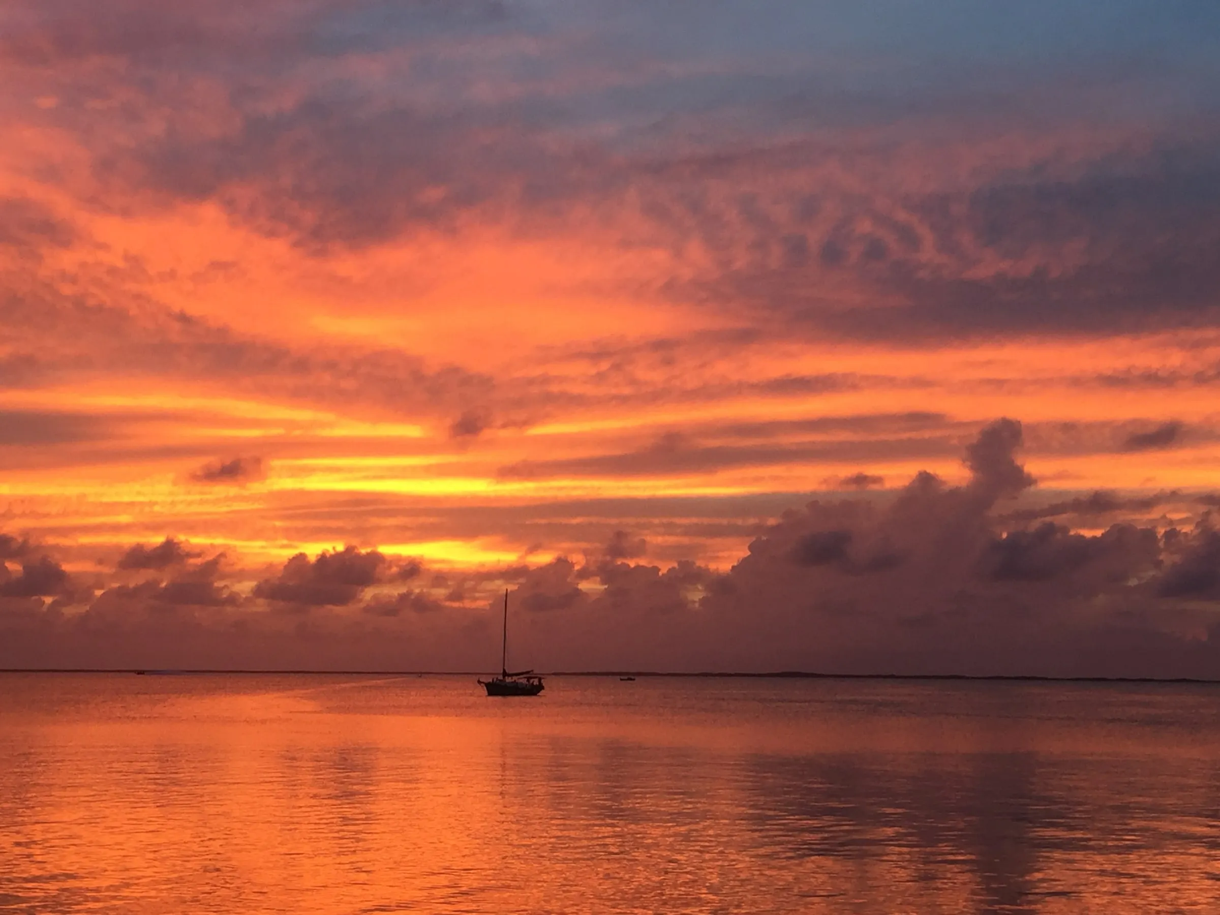 Fiery orange sunset over glassy Florida Bay, with a lone sailboat on the horizon