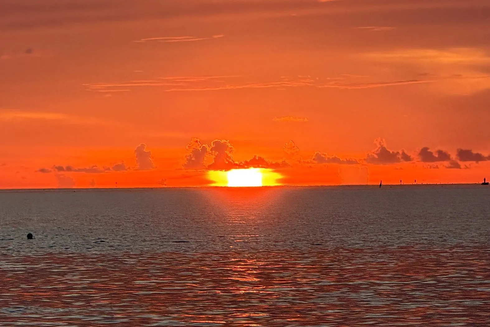 The sun setting on the ocean horizon under an orange sky, seen from the boat on the way to Alligator Reef