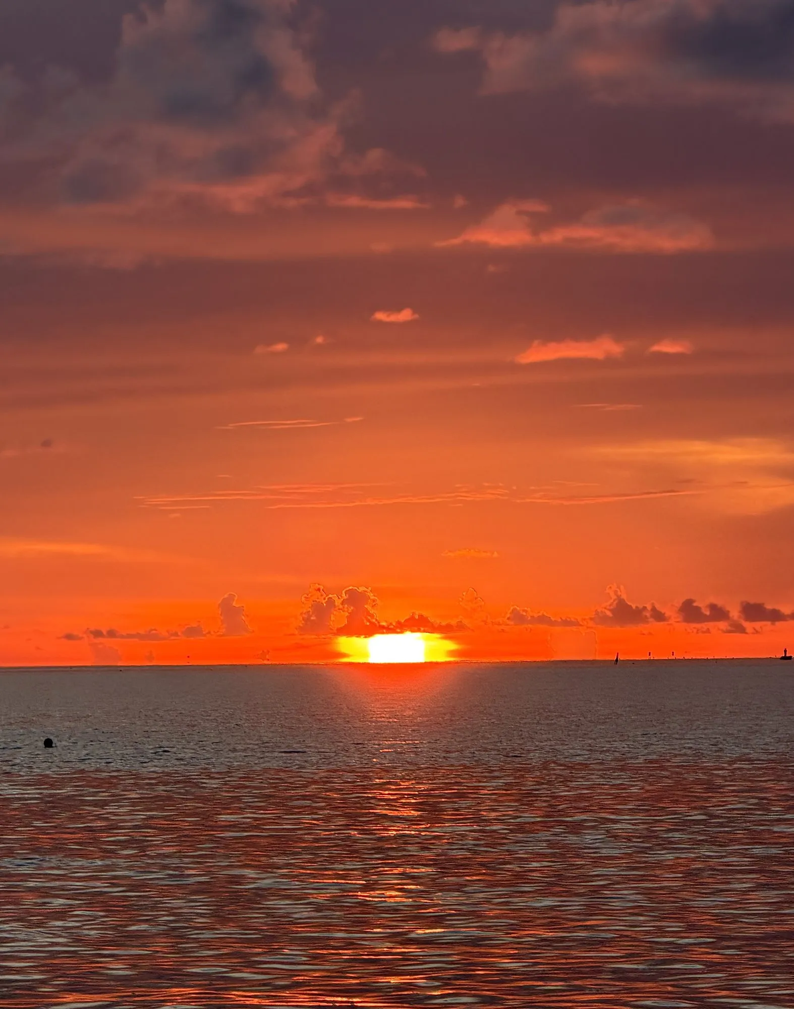 The sun setting on the ocean horizon under an orange sky, seen from the boat